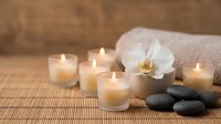 Spa wellness still life with lit candles, white orchid, zen stones, and soft towel on bamboo mat for relaxation therapy.