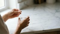 Woman hands holding white ceramic coffee cup or tea mug in bright kitchen interior with natural window light creating cozy morning atmosphere.
