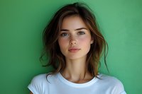 Young Caucasian woman with natural makeup and tousled brown hair wearing white t-shirt against green background, looking directly at camera with confident expression.