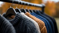 Cozy knitted sweaters in autumn colors hanging on rack, selective focus on warm wool garments showing detailed cable knit texture and natural fibers.