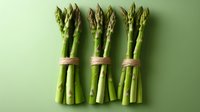 Fresh green asparagus bundles tied with twine arranged in row on mint green background, minimalist food photography composition for healthy eating concept.