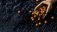 Wooden scoop with mixed black and yellow peppercorns scattered on dark textured surface, dramatic lighting highlights spice texture and natural contrast.