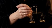 Hands holding golden scales of justice symbolizing law, legal system, fairness and judicial balance in courtroom setting.