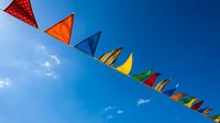 Colorful triangular bunting flags hanging against bright blue sky with white clouds creating festive outdoor celebration atmosphere for parties and events.