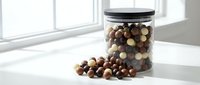 Mixed chocolate balls in glass jar with black lid on white surface near window, scattered candies, natural lighting for food photography and kitchen decor.