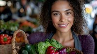 Young African American woman with curly hair smiling while holding fresh organic vegetables at farmers market. Wearing purple sweater and apron as vendor or small business owner.