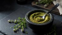 Fresh green herb pesto sauce in stone mortar with pestle and thyme sprigs on dark slate surface for culinary cooking and food preparation.