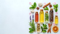 Natural essential oils in glass bottles with fresh herbs, spices and dried citrus on white background for aromatherapy and wellness products.