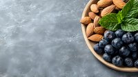 Fresh blueberries and raw almonds in wooden bowl with mint leaves on gray concrete background, healthy snack concept with copy space.
