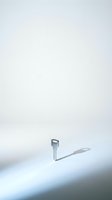 Single metal key standing upright on white surface casting shadow in minimalist composition for security and access concepts.