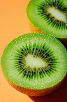 Fresh juicy kiwi fruit halves showing detailed inner texture and seeds on vibrant orange background, macro photography with water droplets for food design.