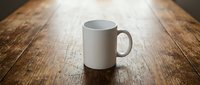 White ceramic coffee mug on rustic wooden table surface with warm lighting for kitchen and dining mockup designs.