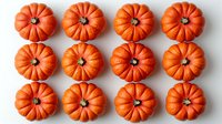 Rows of bright orange mini pumpkins arranged in neat grid pattern on white background, creating minimalist autumn composition for seasonal decor and harvest themes.