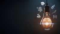 Glowing lightbulb with brain filament surrounded by floating business icons on dark background representing innovation, creativity and entrepreneurial ideas.