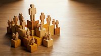 Wooden human figures arranged in a hierarchical pyramid structure on blocks, representing leadership, team management, and organizational chart concepts.