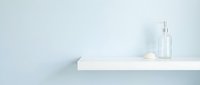 Minimalist white shelf with empty glass bottle and folded towel against pale blue wall, suitable for spa, wellness, and home decor designs.