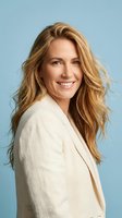 Confident blonde businesswoman smiling in cream blazer against blue background for professional corporate headshot and marketing materials.