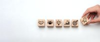 Hand placing wooden blocks with business strategy icons including handshake, teamwork, innovation, growth chart and target goal on white background.