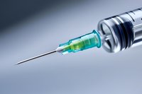 Medical syringe with green liquid and stainless steel needle closeup on gray background, sharp focus on needle tip for healthcare and vaccination concept.