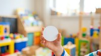 Child's hand holding white sphere toy in playroom with colorful blocks and educational toys in background, suitable for early childhood development and learning concepts.