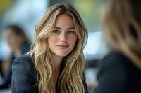 Young blonde woman with natural makeup and wavy hair smiling warmly during business meeting. Professional female executive in gray blazer displaying confident expression.