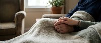 Person relaxing at home wrapped in cozy knit blanket by sunny window. Comfort, wellness, self-care and peaceful indoor lifestyle concept.