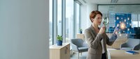Professional businesswoman examining data through magnifying glass in modern office environment for analysis and research purposes.