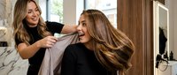 Professional hairstylist styling client's long brown hair in modern salon with natural lighting and contemporary interior design.