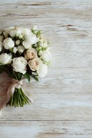 Elegant bouquet of white and cream roses tied with ribbon on rustic whitewashed wooden background with copy space for wedding or celebration design.