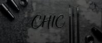 Flat lay composition featuring the word chic written in script with black makeup brushes, cosmetics and beauty products arranged on textured gray surface for fashion and lifestyle design.