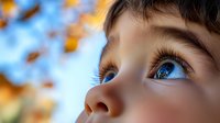 Close-up portrait of child's bright blue eyes gazing upward with wonder against autumn sky background, capturing innocence and curiosity in natural lighting.