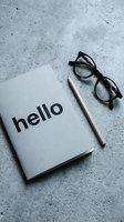 Minimalist notebook with hello text, pencil, and glasses on gray concrete surface, flat lay for business or education concepts.