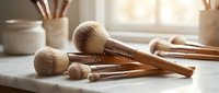 Professional makeup brushes with wooden handles arranged on white marble surface in bright natural light for beauty and cosmetics applications.