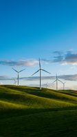 Wind turbines on rolling green hills under blue sky with clouds at sunset, representing renewable energy and sustainable power generation for environmental projects.