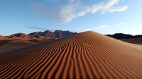 Rippled sand dunes stretch across desert landscape at sunset, dramatic mountain range silhouette in background against blue cloudy sky, natural patterns in sand.