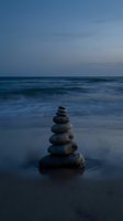 Zen stone stack balanced on wet beach sand at twilight with calm ocean waves and moody blue sky creating peaceful meditation atmosphere.
