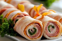 Rolled turkey and ham pinwheels with cream cheese, fresh herbs and cheddar slices arranged on white plate, macro food photography for appetizer menu.