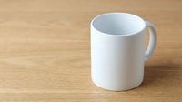 White ceramic coffee mug on wooden table surface for branding mockup and promotional design projects.