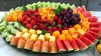 Fresh fruit platter with watermelon, cantaloupe, honeydew, strawberries, grapes and oranges arranged in colorful rows on round serving tray for party or catering.