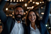 Happy business team celebrating success with raised arms and bright smiles in modern office with warm lighting atmosphere for corporate achievement concepts.