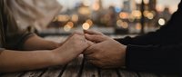 Couple holding hands tenderly on a wooden table with a blurred city skyline at dusk, capturing love, connection, and romance.