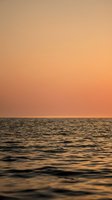Serene ocean waves reflecting warm golden sunset colors creating peaceful seascape with soft orange and peach sky gradient for relaxation backgrounds.