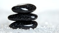 Stacked black spa stones on crystal salt background with water drops, creating zen balance composition for wellness and meditation atmosphere.