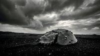 Dramatic black and white landscape featuring large weathered boulder on rocky terrain under moody stormy sky with heavy clouds for nature photography.