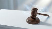 Wooden judge gavel with digital legal technology icons and holographic interface elements on white desk representing modern law practice and justice system.