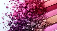 Crushed eyeshadow palette swatches in gradient from pink to purple shades with scattered powder and shimmer particles on light background. Makeup artistry concept.