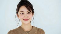 Young Asian woman with updo hairstyle and soft smile wearing beige sweater against light background, portraying warmth and approachability.
