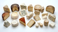 Assorted artisanal cheese varieties including aged cheddar, soft brie, blue cheese, and specialty selections displayed on white background for culinary and food styling projects.
