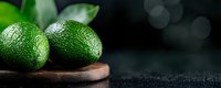 Fresh whole green limes with textured peel on rustic wooden board against dark background with bokeh lights, macro food photography with copy space.