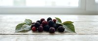Fresh blackberries with green leaves arranged on rustic white wooden surface, suitable for food photography, recipe blogs, and culinary design projects.